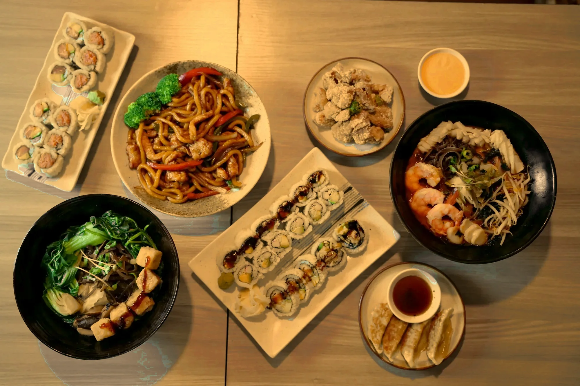 A full table seen from above: ramen, yaki udon, sushi rolls, gyoza and karaage