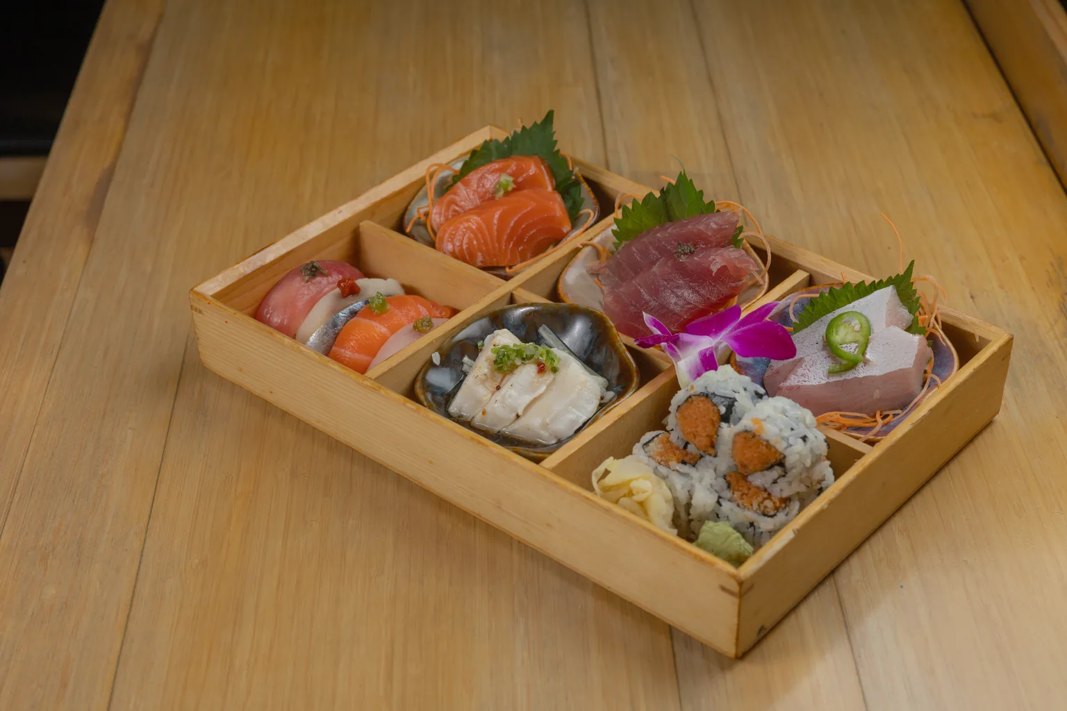 A wooden box of salmon, tuna and yellowtail sashimi with sushi rolls
