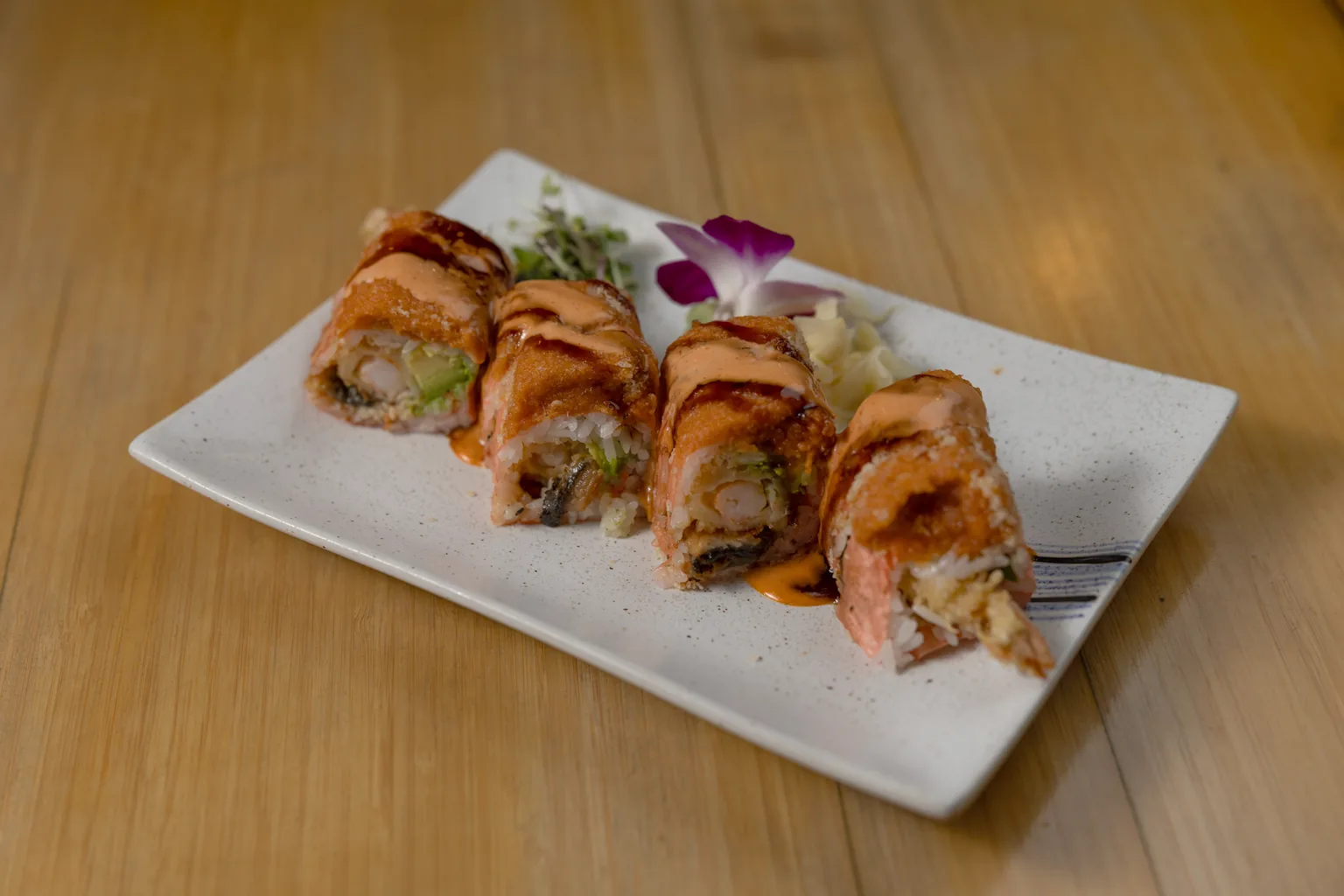 A seared special roll with spicy mayo, eel sauce and an orchid